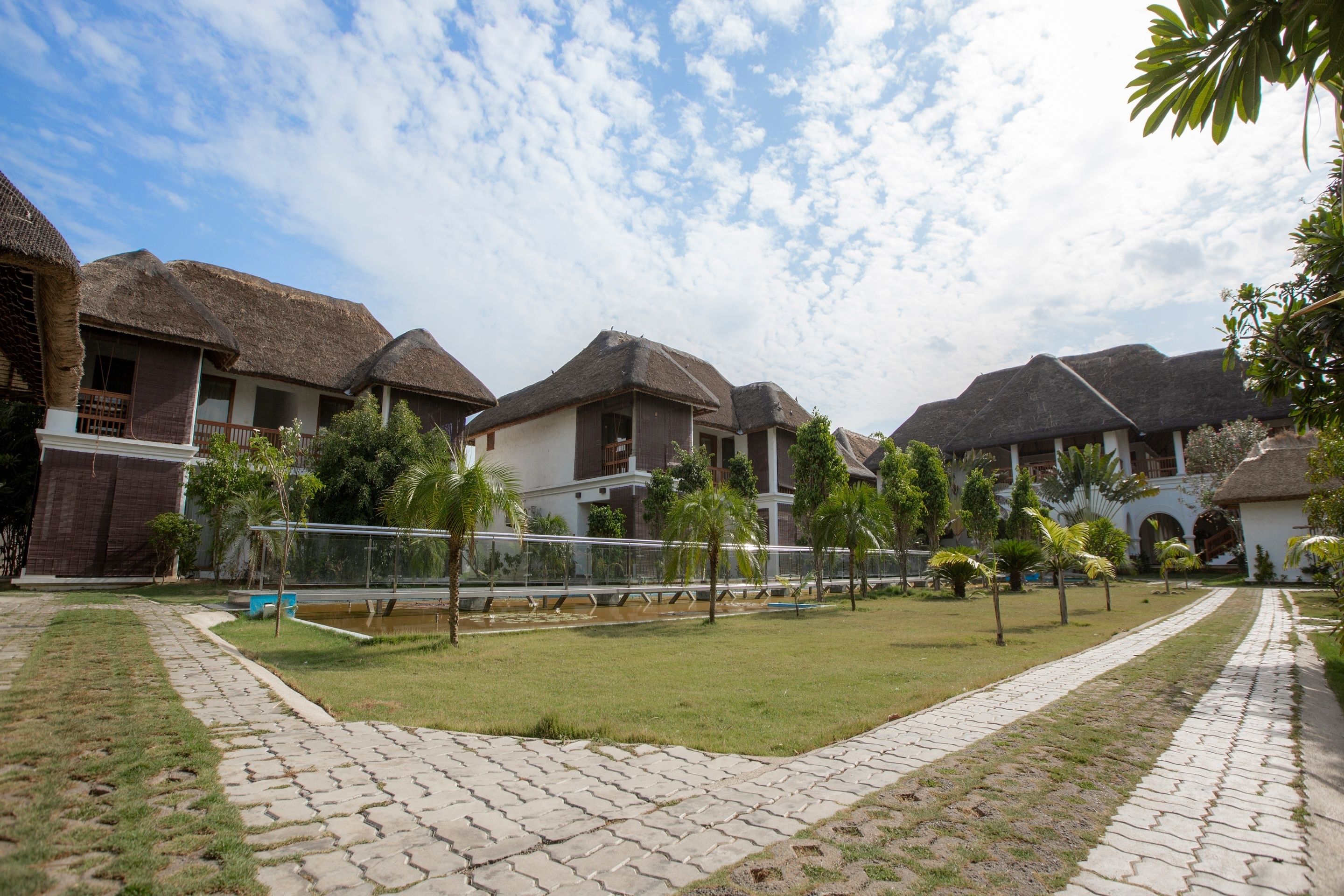 A resort with thatched-roof cottages, paved walkways, and a well-maintained lawn.