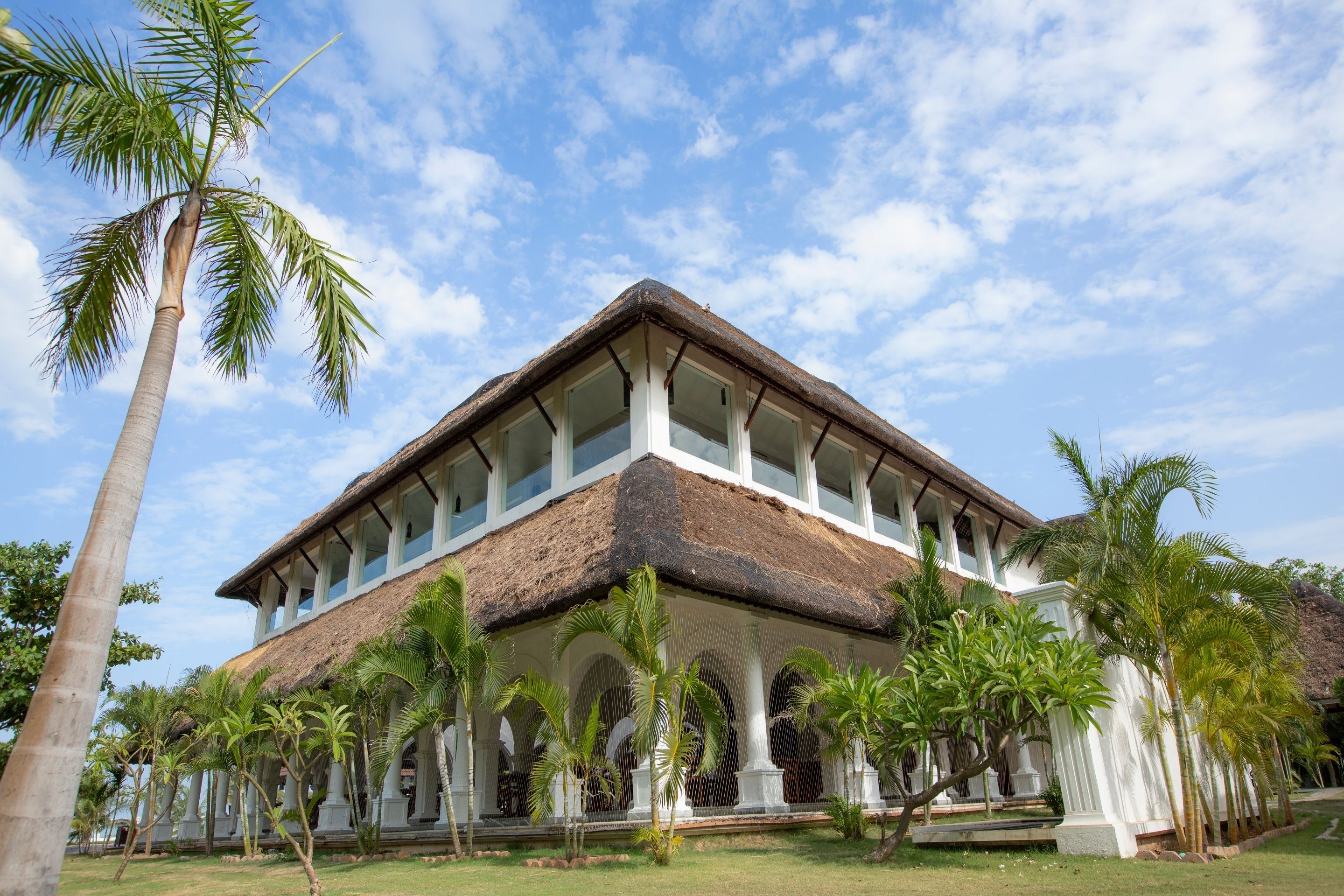 A large building with a thatched roof, multiple columns, and a covered walkway with palm trees.
