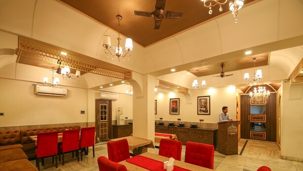 A restaurant with red upholstered chairs and tables, a bar area, and a ceiling fan. - Hotel Datt Residency (Jabalpur)