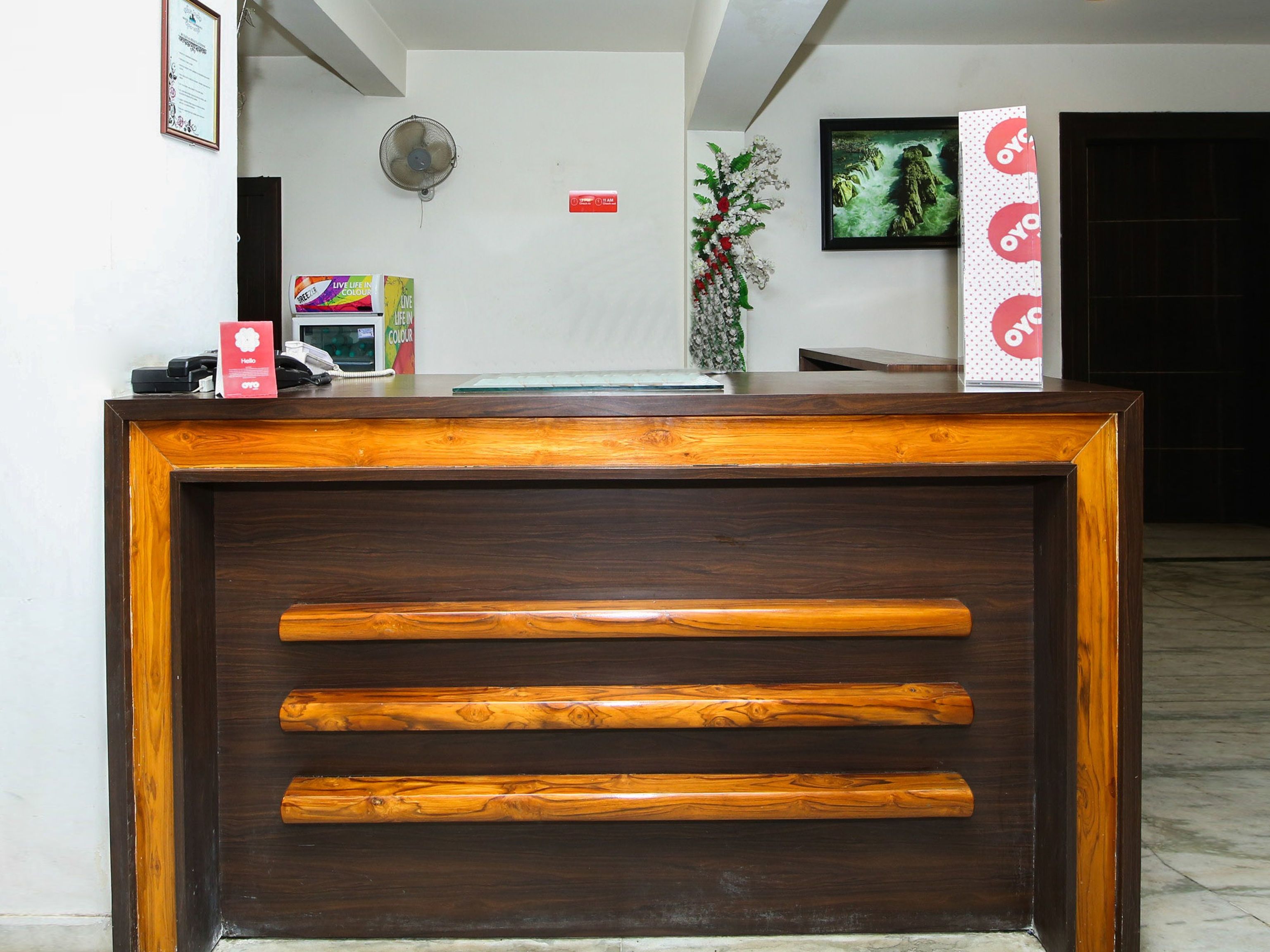Un mostrador de recepción con detalles de madera, un ventilador fijado a la pared, un certificado enmarcado y un cuadro en la pared.