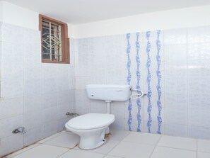 A small, basic bathroom with a toilet, a window with metal bars, and patterned tiles.