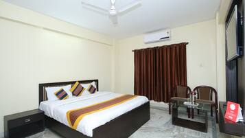 A hotel room with a bed, a desk, a chair, a ceiling fan, an air conditioning unit, and a window with curtains.