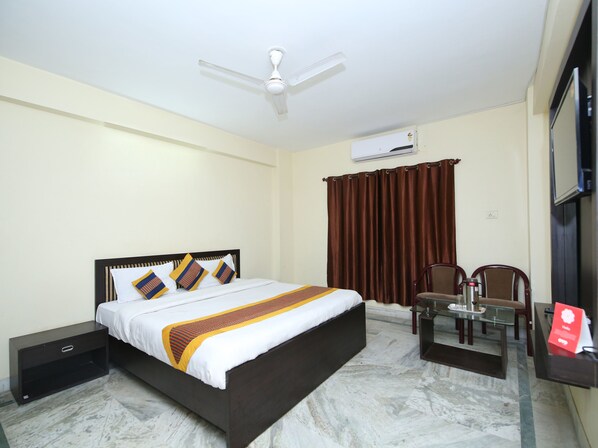 A hotel room with a bed, a desk, a chair, a ceiling fan, an air conditioning unit, and a window with curtains.