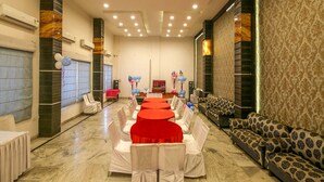 A banquet hall with round tables covered in red tablecloths, white chairs, and a patterned sofa. - Hotel Datt Residency (Jabalpur)