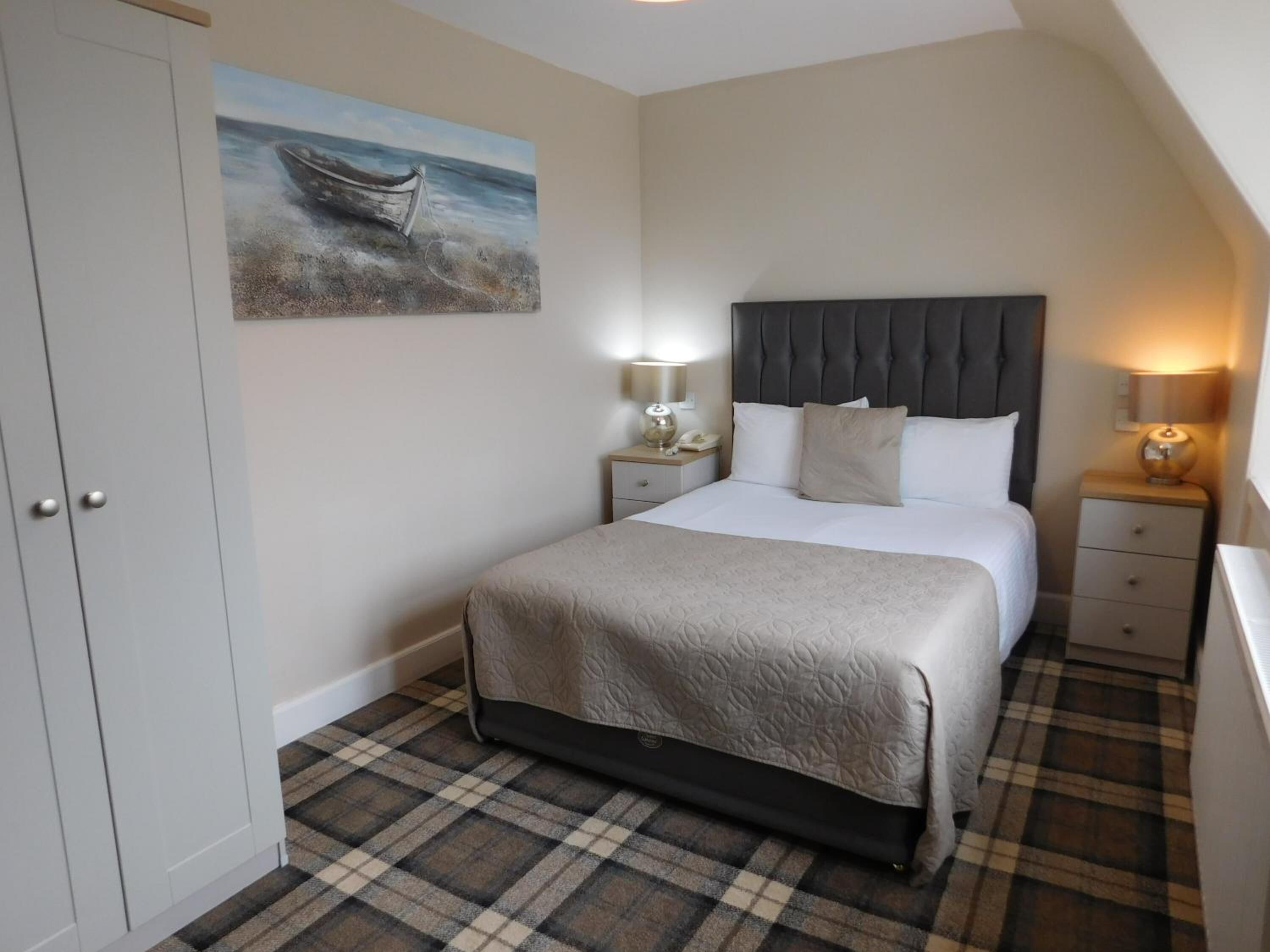 A bedroom with a bed, a nightstand, a bedside lamp, a painting on the wall, and a wardrobe.