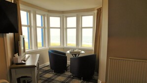 A corner room with a checkered carpet, two black chairs, a small round table, a desk with a telephone, and a window with curtains. - Cullen Bay Hotel (Buckie)