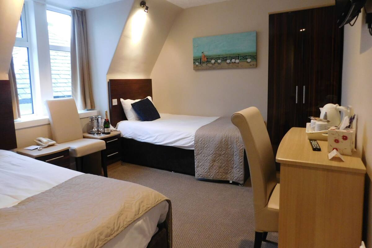A hotel room with two beds, a desk, a chair, a nightstand, a painting on the wall, and a wardrobe.