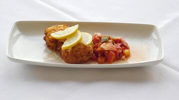 A rectangular white plate with two breaded patties and a tomato-based sauce, garnished with lemon slices.