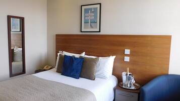 A hotel room with a large bed, a wooden headboard, a bedside table with a bottle of champagne, a mirror, and a framed picture on the wall.