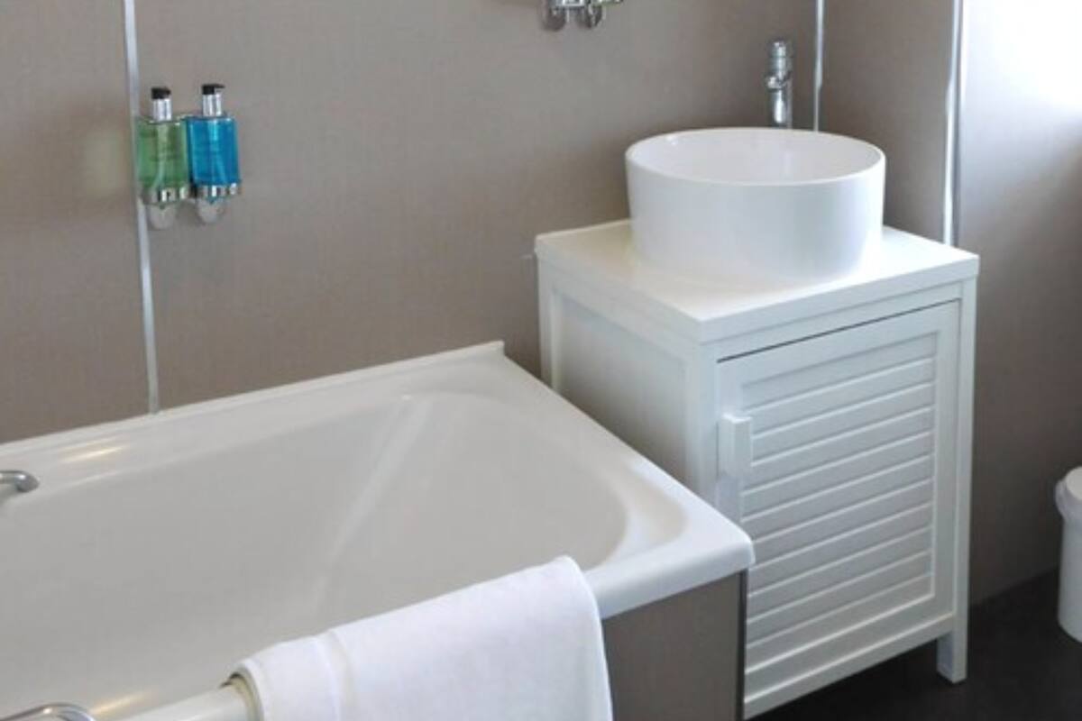 A bathroom with a white bathtub, a white sink on a cabinet, and a towel hanging on the tub.