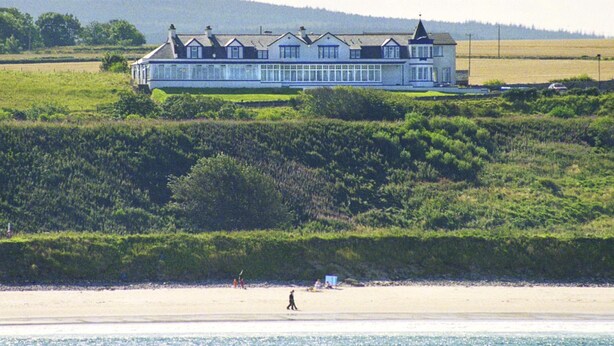 A large, multi-story house with a prominent balcony, situated on a hill overlooking a beach. - Cullen Bay Hotel (Buckie)