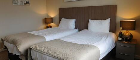 A double room with two beds, a wooden headboard, bedside tables with lamps, and a painting on the wall.