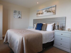 A neatly arranged bedroom with a large bed, a nightstand with a bottle of champagne, and a framed artwork on the wall. - Cullen Bay Hotel (Buckie)