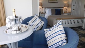 A bedroom with a bed, bedside tables, a nightstand, a bedside lamp, a framed picture on the wall, and a bottle of champagne on a tray. - Cullen Bay Hotel (Buckie)