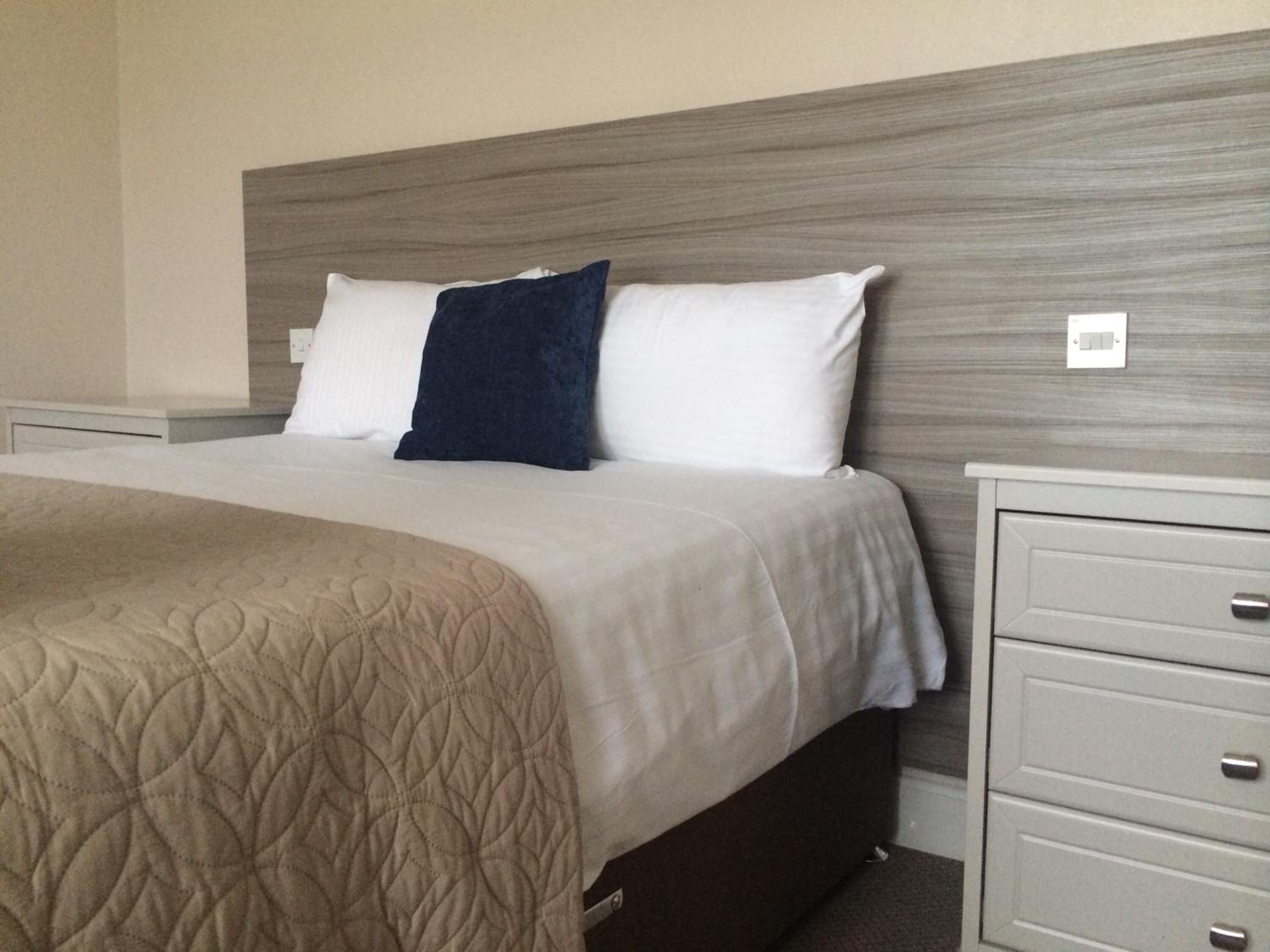 Quarto de hotel com cama, mesa de cabeceira e cômoda.