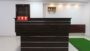 A reception desk with a digital clock displaying 12 PM and 11 AM, a ceiling fan, and a framed religious painting on the wall. - OYO 15776 V R Residency (Bengaluru)