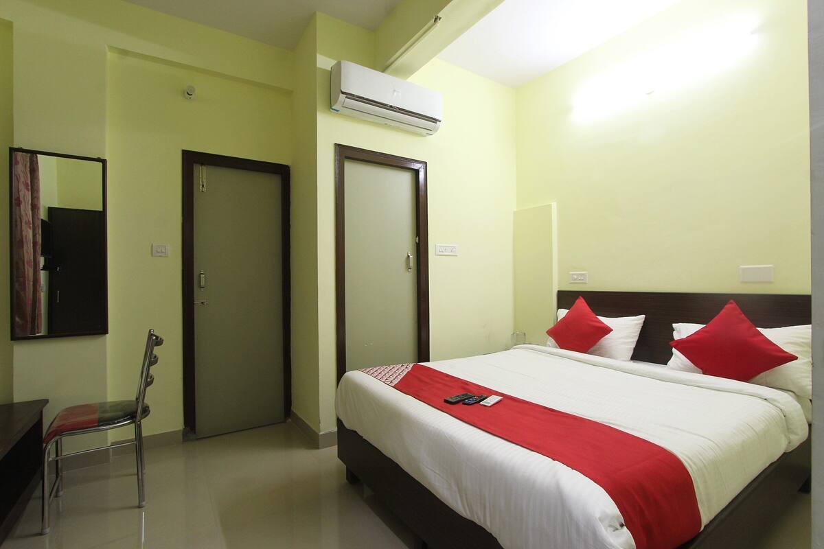 A hotel room with a bed, a chair, a desk, and an air conditioning unit.