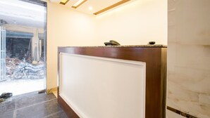 A reception desk with a marble floor, a glass door leading outside, and a ceiling with recessed lighting. - OYO 16375 Melfort Inn (New Delhi)