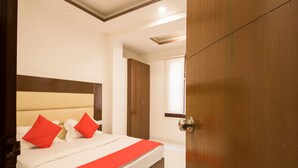A hotel room with a bed, a wooden wardrobe, and a door. - OYO 16375 Melfort Inn (New Delhi)