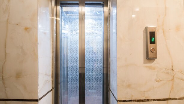 An elevator with a patterned glass door and a digital control panel on the wall. - OYO 16375 Melfort Inn (New Delhi)