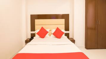 A neatly made bed with a red accent, a wooden wardrobe, and a bedside table with a phone.