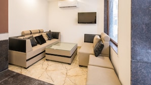 A modern living room with a sectional sofa, a glass coffee table, and a flat-screen TV mounted on the wall. - OYO 16375 Melfort Inn (New Delhi)