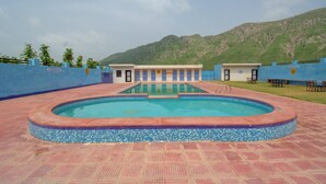 A swimming pool with a tiled edge, surrounded by a blue wall and a mountain backdrop.