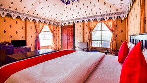 A large bed with red pillows, a television, and a desk in a room with patterned walls and curtains.