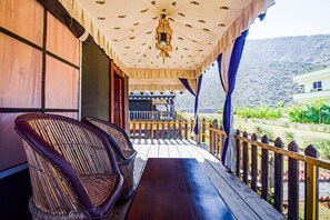 A wooden deck with wicker chairs and a table, overlooking a garden and a mountain. - OYO 16709 Green Valley Resort (Ajmer)