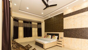 A bedroom with a bed, a ceiling fan, a wardrobe, and a seating area with a wooden bench. - OYO 16593 Home Luxury 3BHK Galaxy Villa Andrar (Dharamshala)