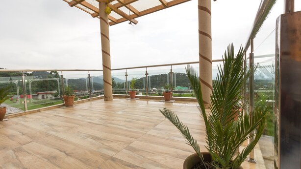 A spacious balcony with wooden flooring, potted plants, and a view of distant mountains. - OYO 16593 Home Luxury 3BHK Galaxy Villa Andrar (Dharamshala)