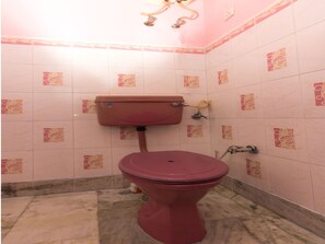 A bathroom with a pink toilet, white tiled walls with floral patterns, and a marble floor.