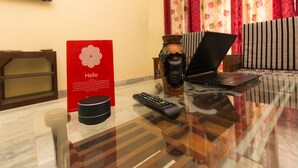 Une chambre d’hôtel avec une table basse en verre, un ordinateur portable, une télécommande, un panneau rouge, un vase décoratif et un canapé à rayures.