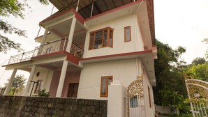 Une maison à deux étages dotée d’un balcon, d’une entrée fermée par un portail et d’un mur en pierre.