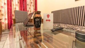 Une pièce avec une table en verre, un ordinateur portable, un vase, une télécommande et un panneau indiquant les chambres OYO.