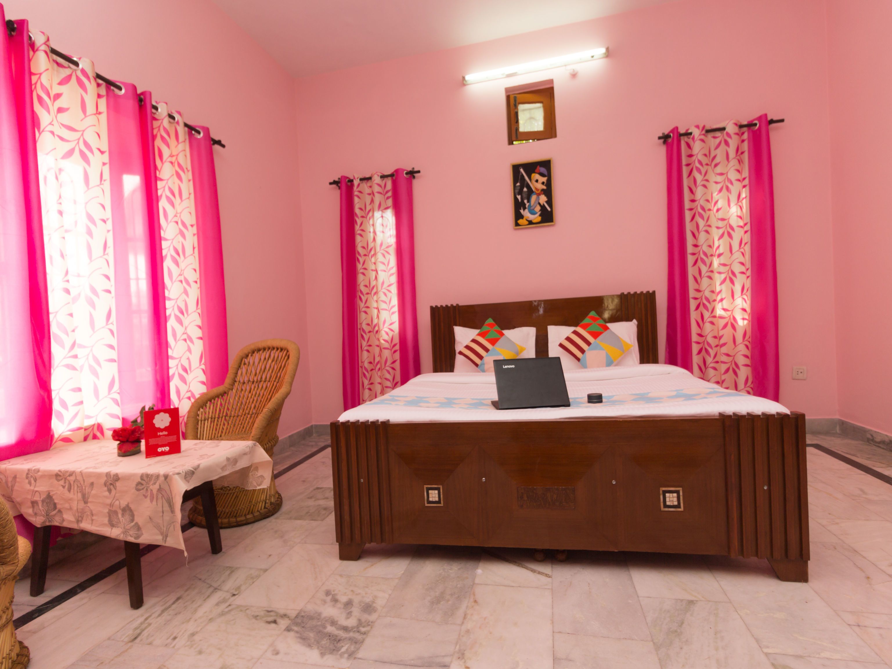 Un dormitorio con decoración rosa, con cama, una silla, una mesa y un ordenador portátil.