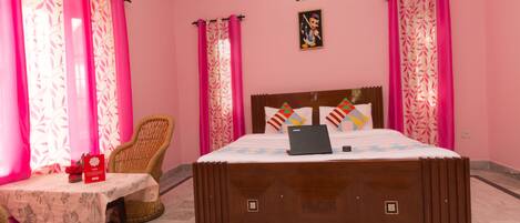 Un dormitorio con decoración rosa, con cama, una silla, una mesa y un ordenador portátil.