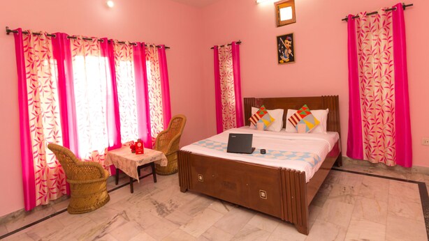 Une chambre à coucher avec un lit, deux chaises, une petite table et des rideaux roses.