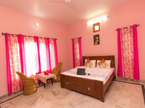 Ein Schlafzimmer mit einem Bett, zwei Stühlen, einem kleinen Tisch und rosa Vorhängen.