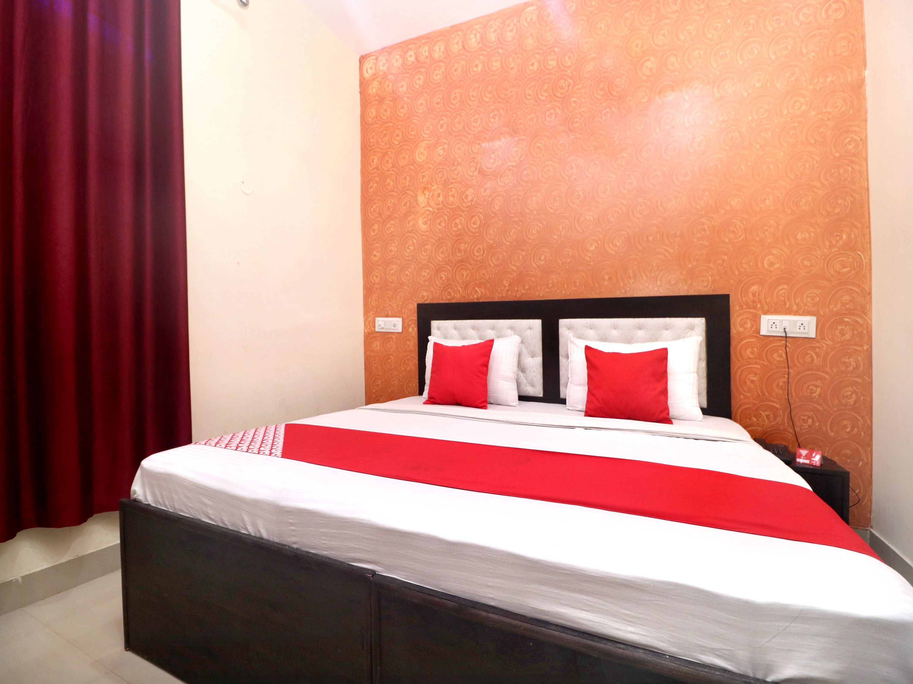 A neatly made bed with a red and white bedspread and two red pillows, set against a wall with a patterned wallpaper.