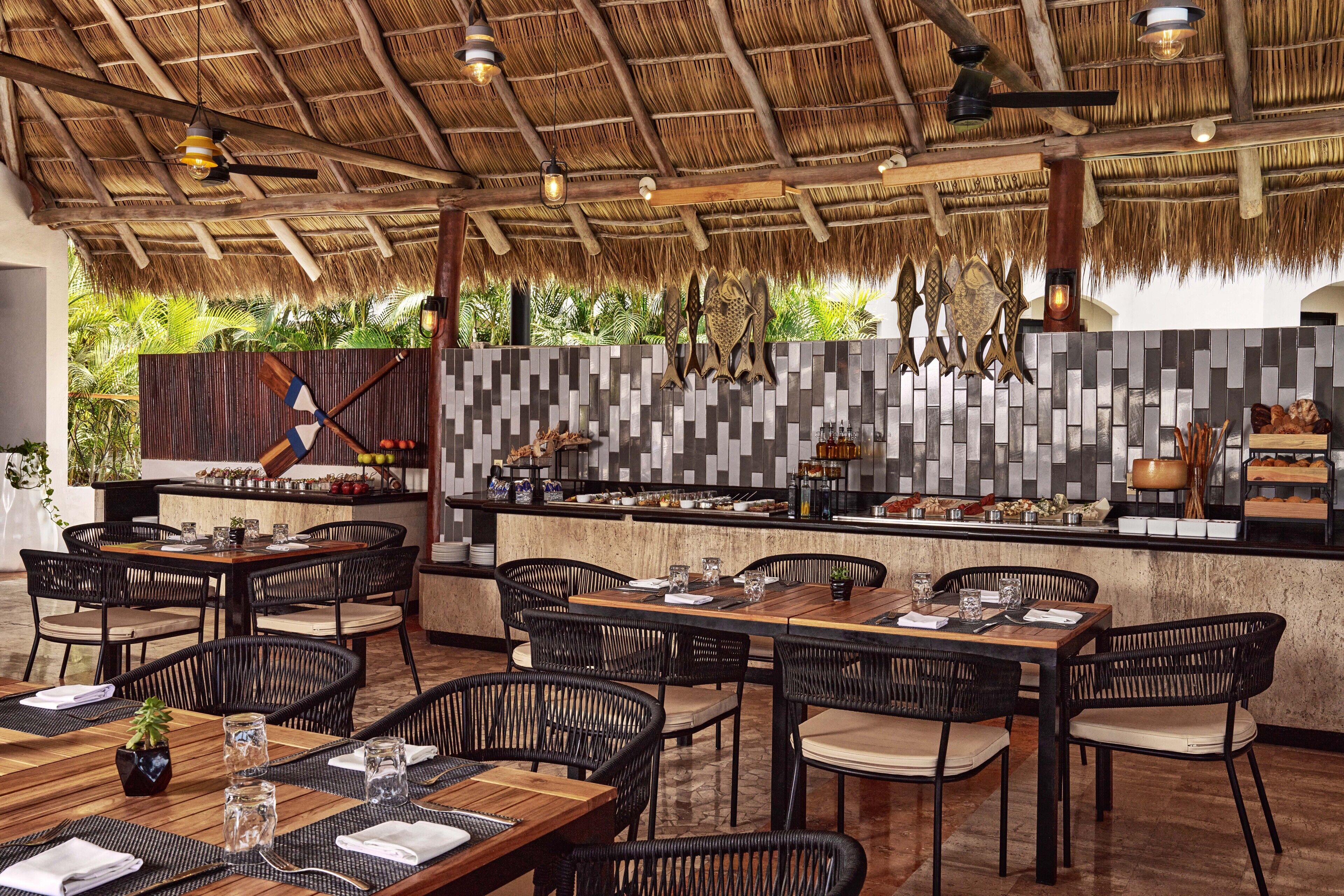 An outdoor restaurant with thatched roof, black wicker chairs, and a tiled backsplash.