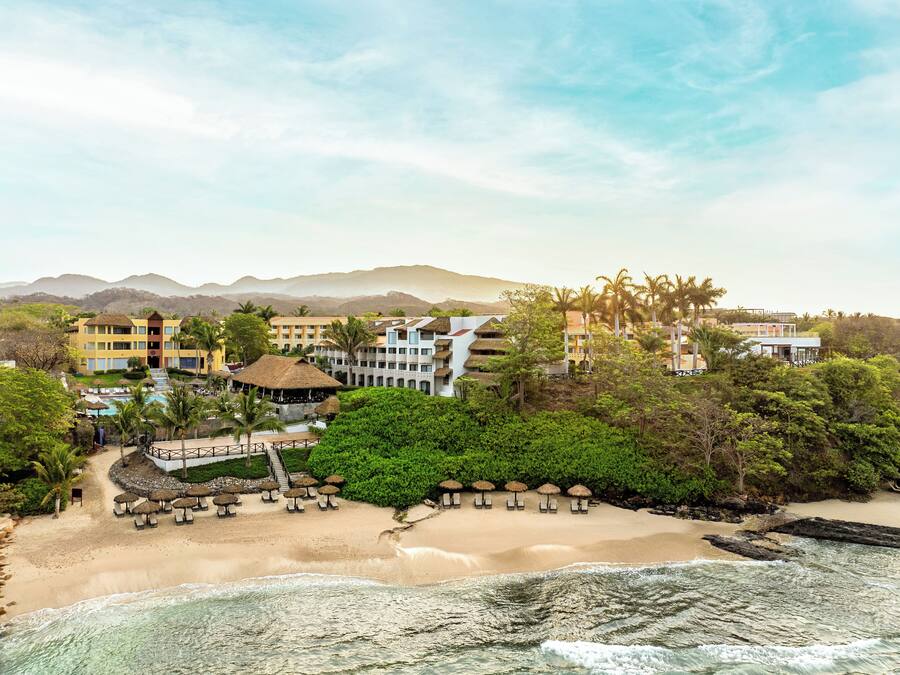 A resort with multiple buildings, a beach, and a mountain backdrop.