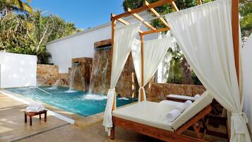 A poolside area with a wooden bed, white curtains, and a small table with towels.
