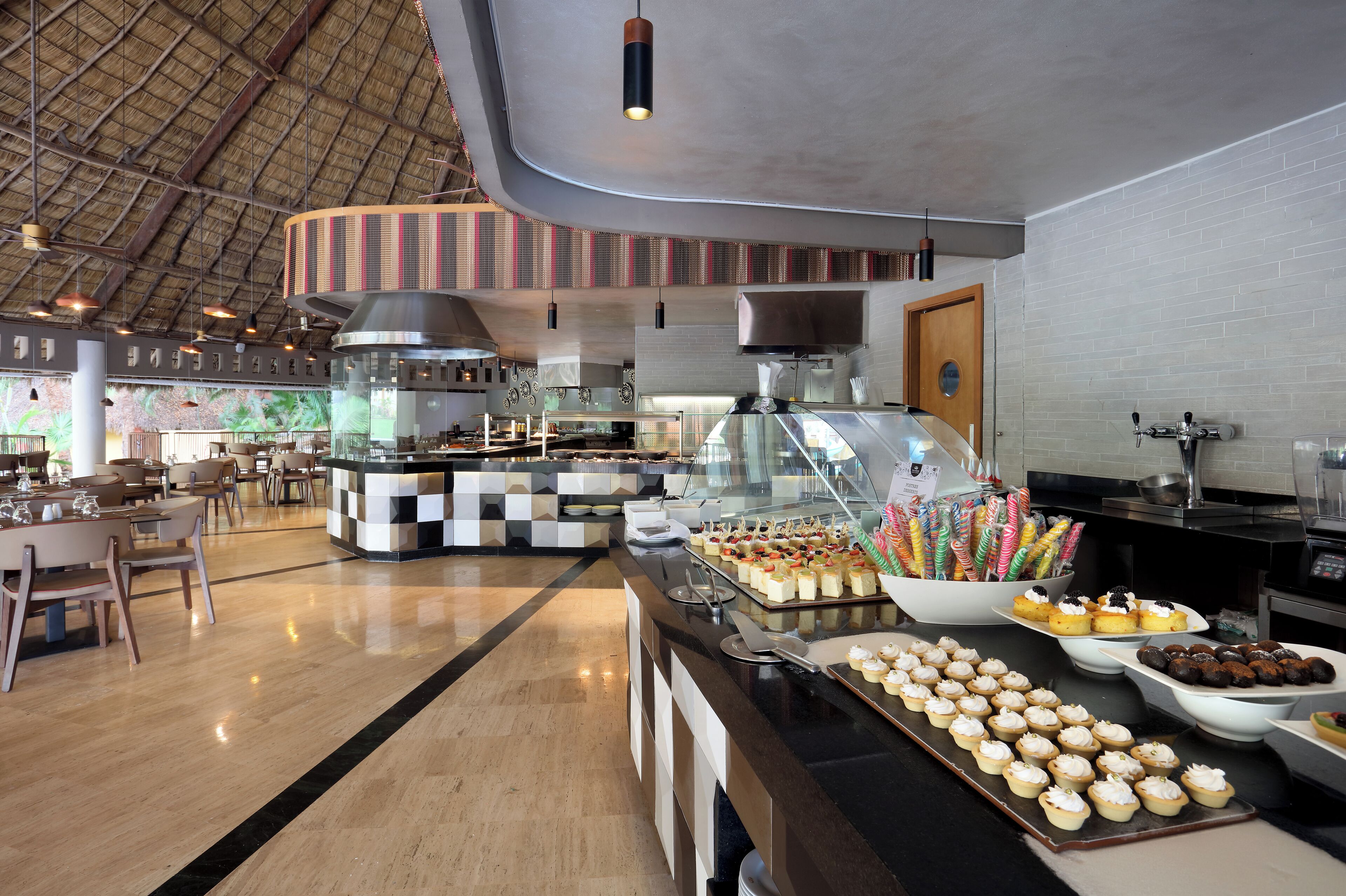 Een buffetgedeelte met diverse gerechten, een keuken op de achtergrond en een hoog plafond met een bijzonder ontwerp.