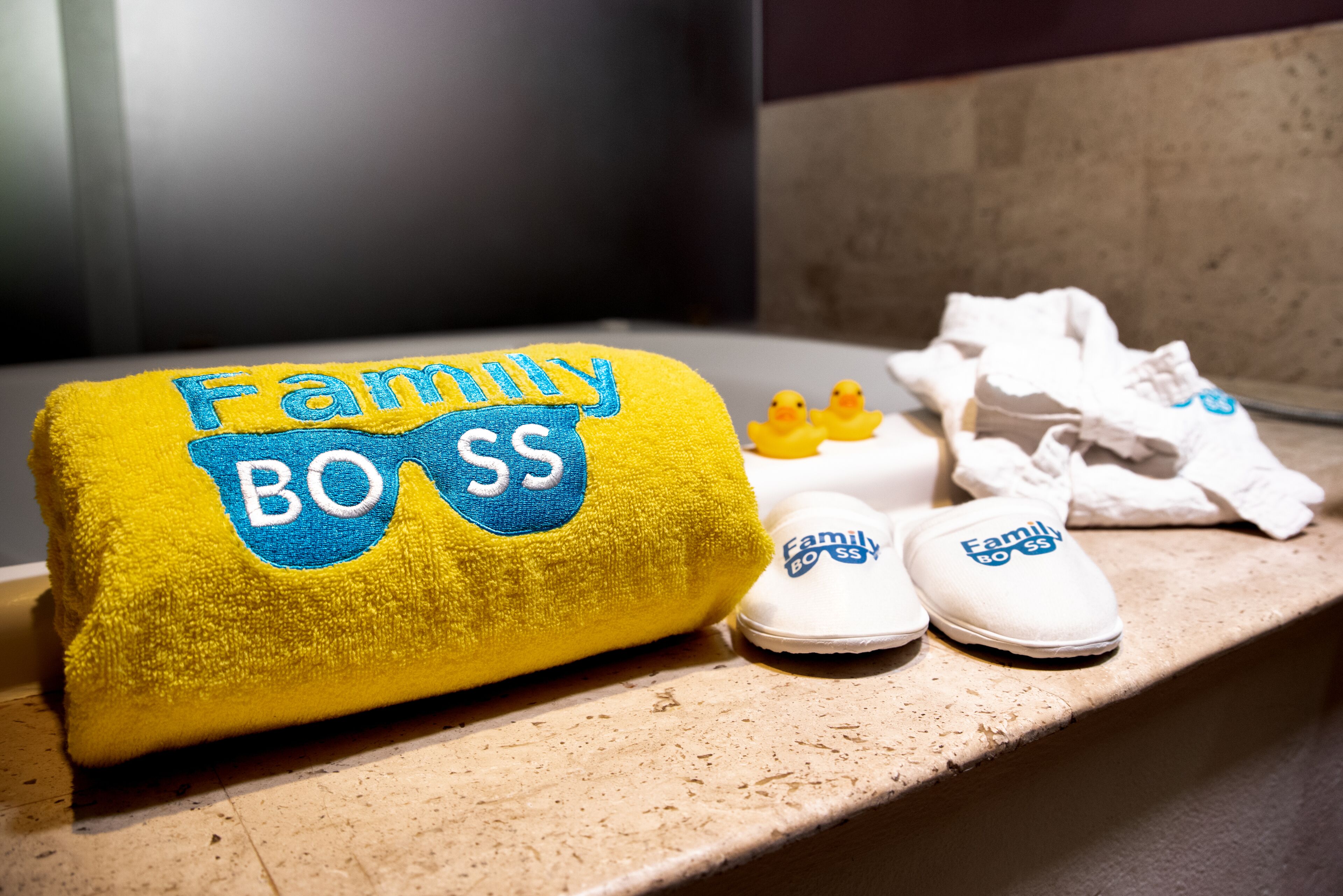 A yellow towel with 'Family Boss' embroidered on it, next to a pair of white slippers with the same text.