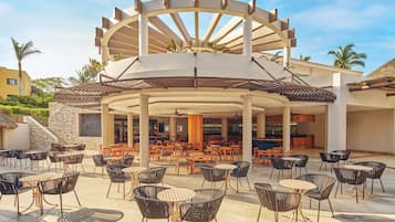 Un patio al aire libre con diversas opciones de mobiliario, incluyendo mesas y sillas redondas, y un elemento arquitectónico central con diseño circular.