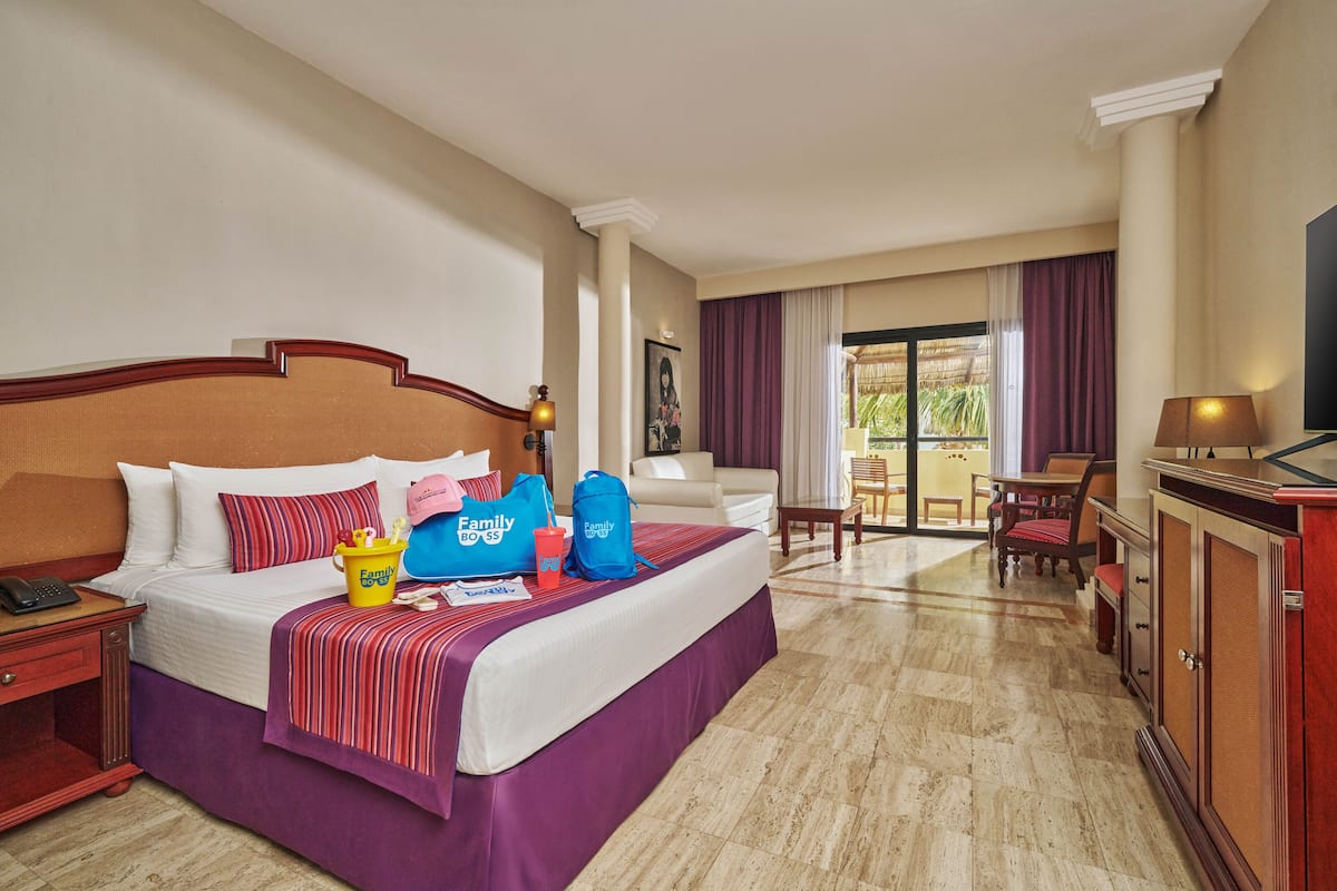 Habitación de hotel con una cama grande, un escritorio, un televisor y un balcón con vistas al exterior.