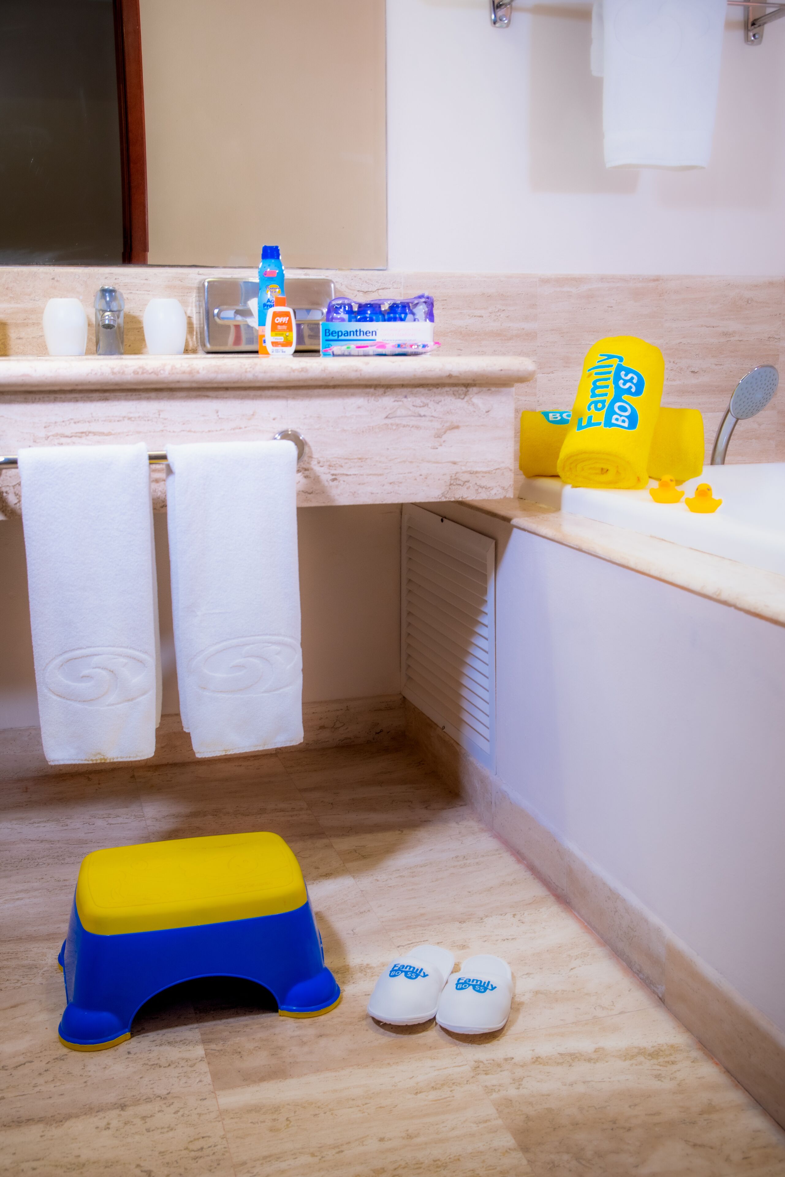 Een badkamer met een wastafel, twee handdoeken, een opstapje en slippers.