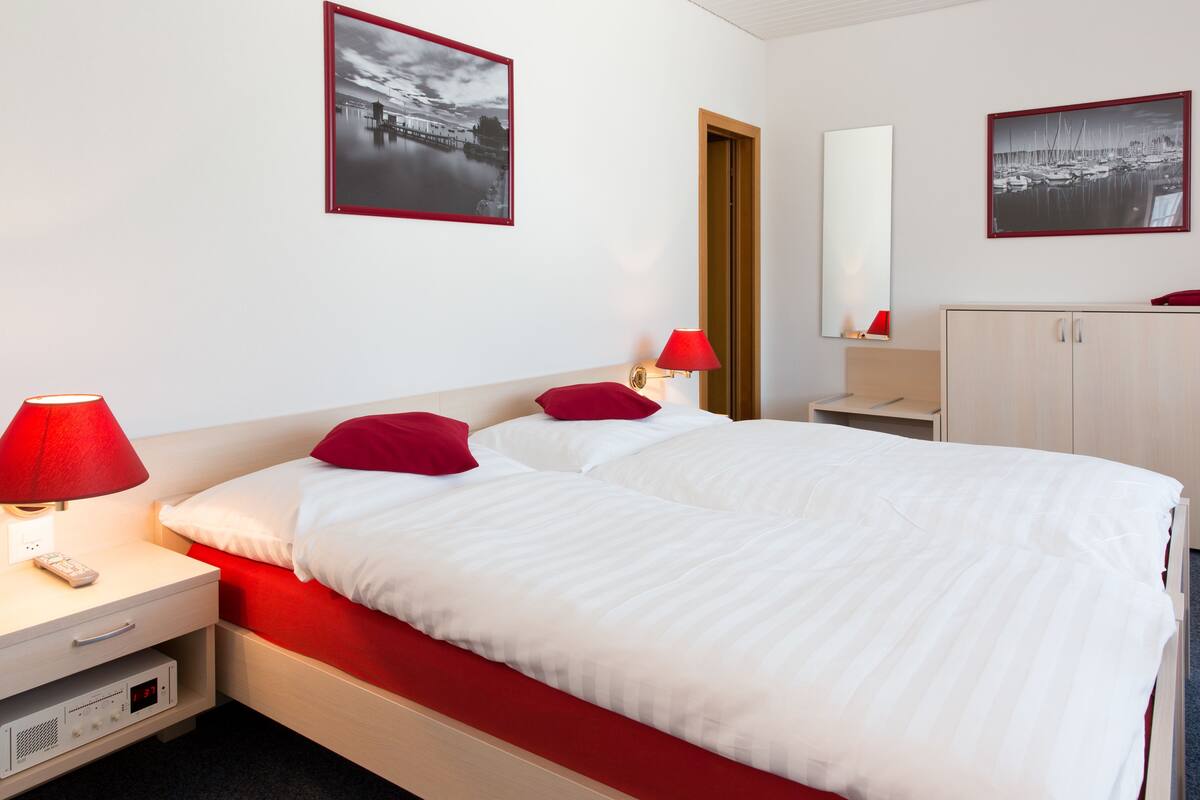 A hotel room with a bed, nightstands, a lamp, a mirror, and two framed pictures on the wall.