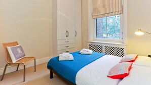 A bedroom with a bed, a chair, a wardrobe, and a window with blinds. - The Chelsea Apartment (London)